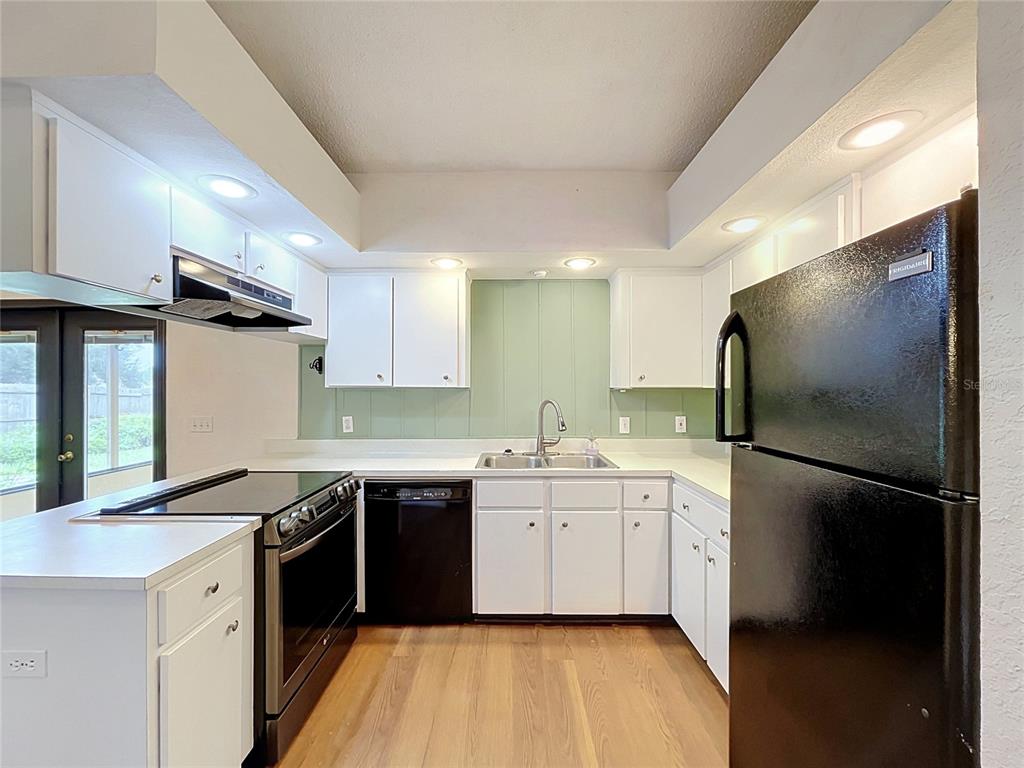 A kitchen features white cabinets, black appliances, a light green backsplash, and wood-look flooring — 3974 LIME TREE LANE, LAKELAND, FL