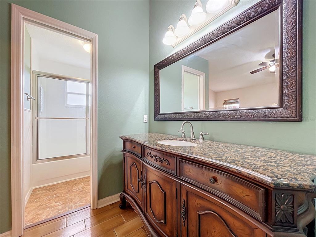 A bathroom features a wooden vanity with a granite countertop, a large mirror, and tile flooring — 3974 LIME TREE LANE, LAKELAND, FL