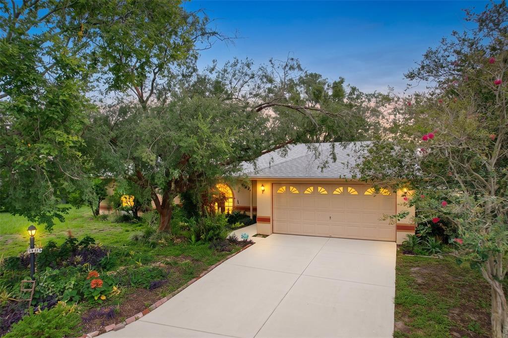 A single-story house with a beige garage, a concrete driveway, and large trees in front — 3974 LIME TREE LANE, LAKELAND, FL