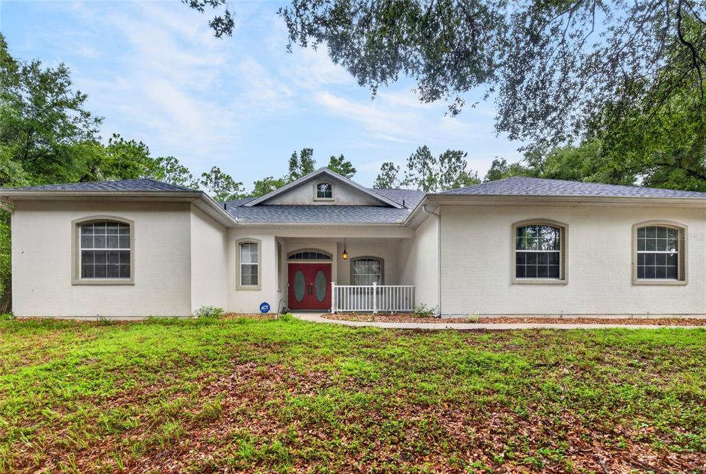 A single-story house with a white stucco exterior, a red front door, and arched windows — 7550 SW 185TH CIRCLE, DUNNELLON, FL