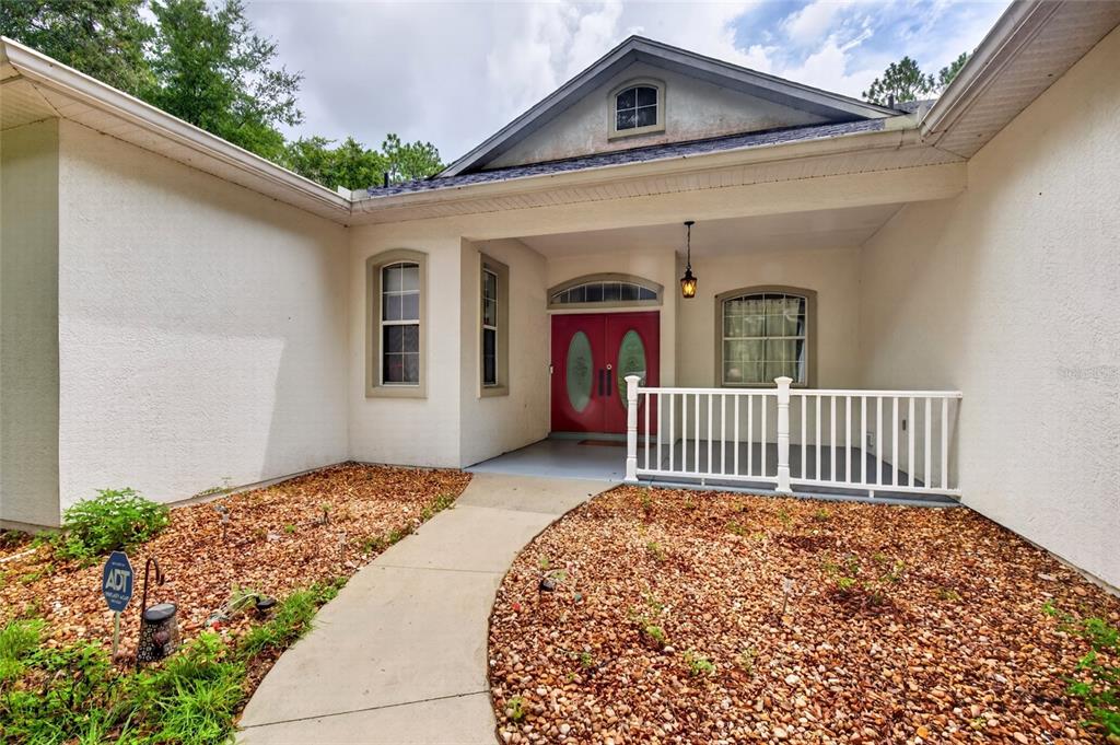 The exterior of a house features a concrete walkway leading to a red double front door — 7550 SW 185TH CIRCLE, DUNNELLON, FL