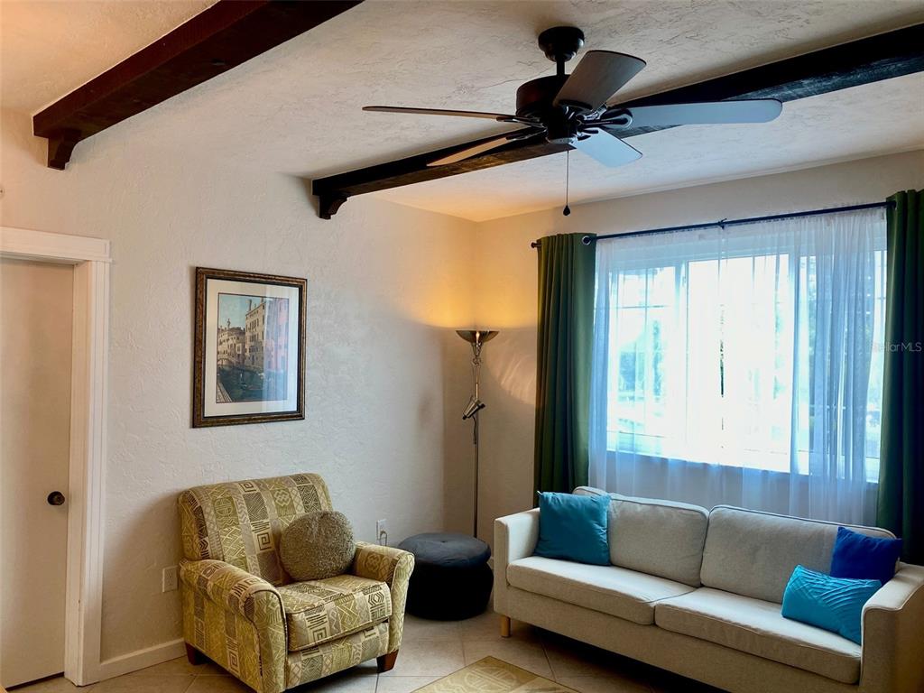 A living room features a beige sofa, a patterned armchair, and exposed dark wood ceiling beams — 238 TAMPA AVENUE W UNIT 6B, VENICE, FL