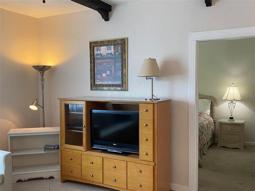 A living room features a wooden entertainment center, a floor lamp, and a doorway to a bedroom — 238 TAMPA AVENUE W UNIT 6B, VENICE, FL