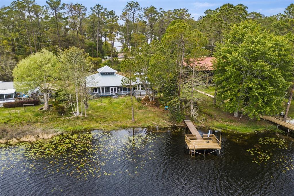 An aerial view shows a house with a metal roof, a wooden dock, and trees — 299 RILEY LAKE DRIVE, HAWTHORNE, FL