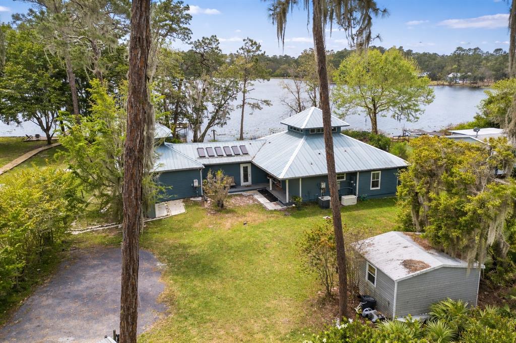 An aerial view of a blue house with a metal roof beside a lake — 299 RILEY LAKE DRIVE, HAWTHORNE, FL