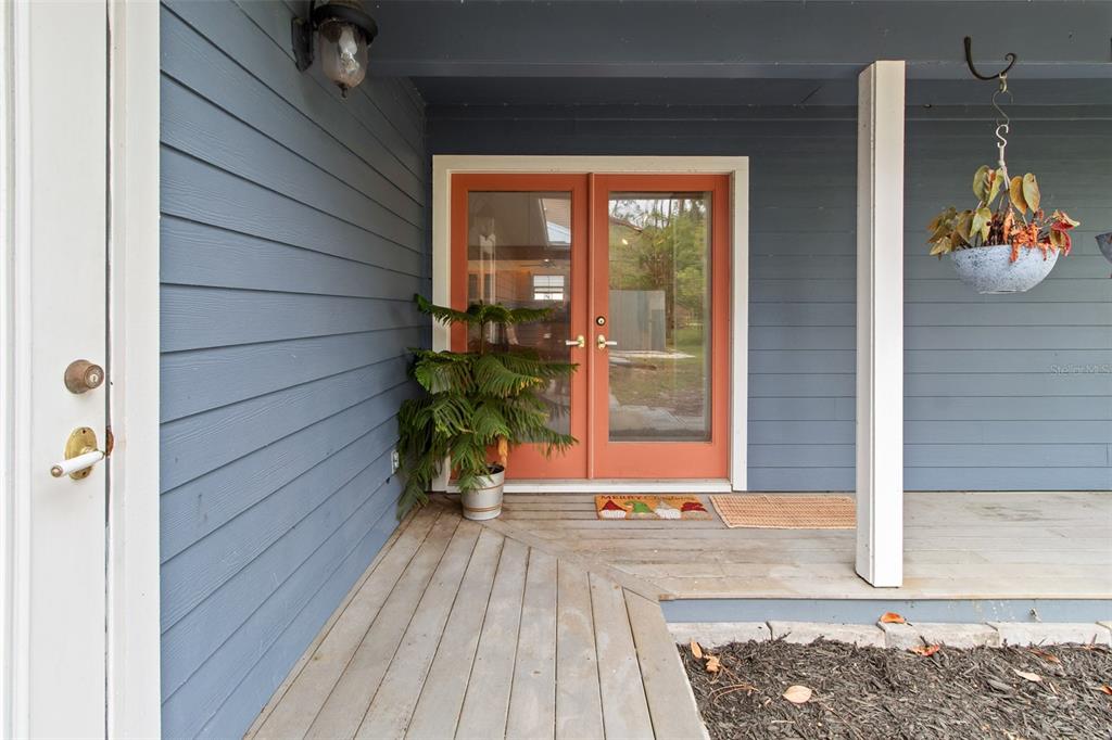 A covered wooden porch features blue siding, orange double doors, and a hanging plant — 299 RILEY LAKE DRIVE, HAWTHORNE, FL