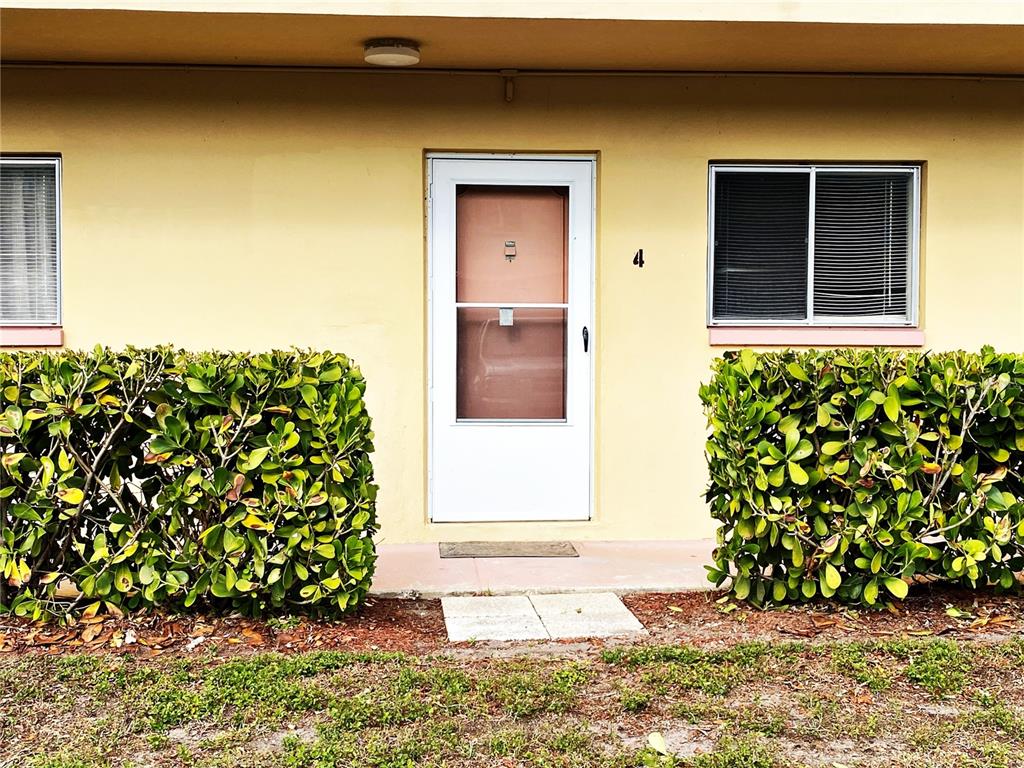 The exterior of a yellow building features a white front door labeled number four — 2003 GREENBRIAR BOULEVARD UNIT 4, CLEARWATER, FL