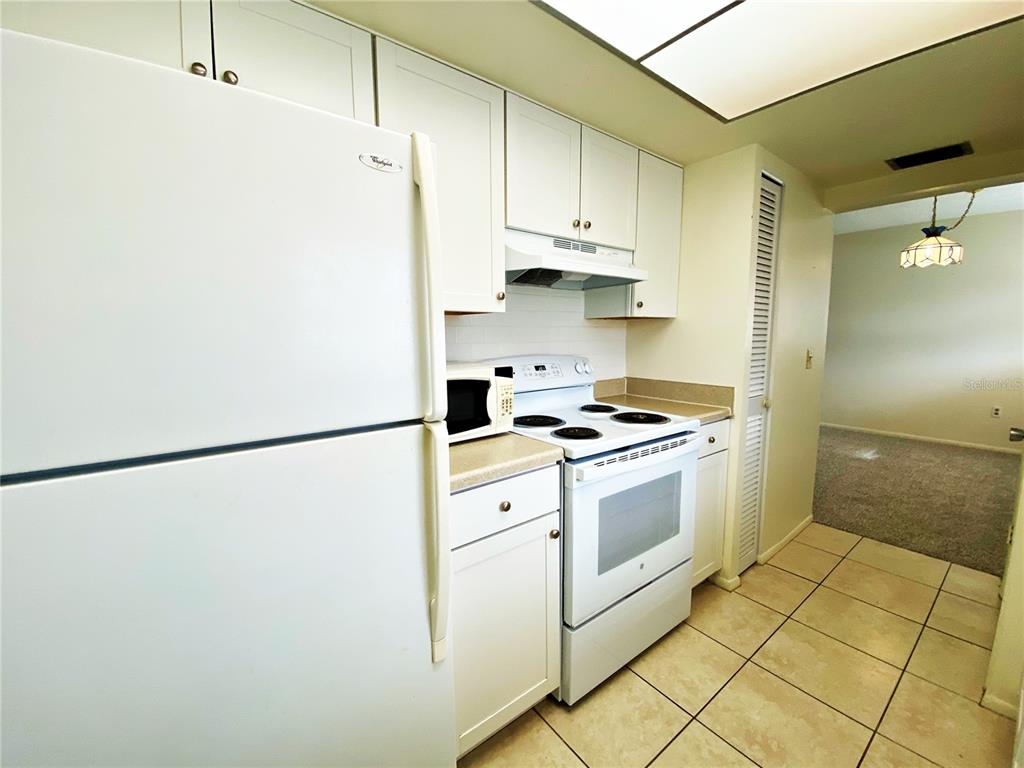 A kitchen features white cabinets, a white refrigerator, a white stove, and tiled flooring — 2003 GREENBRIAR BOULEVARD UNIT 4, CLEARWATER, FL