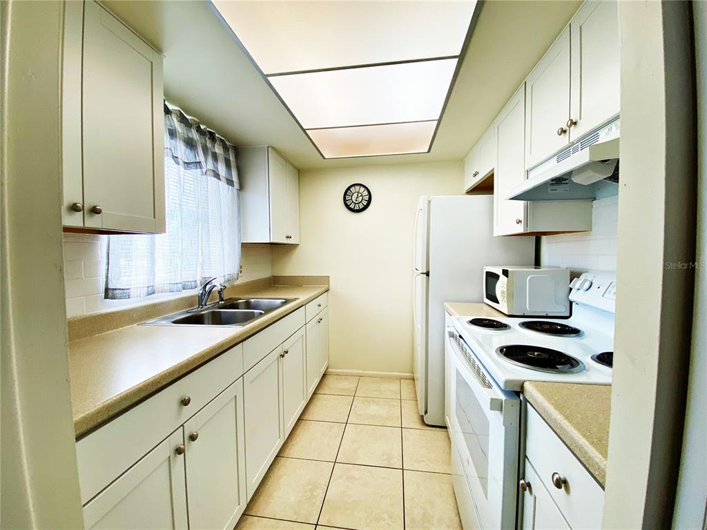 A galley kitchen features white cabinets, beige countertops, a double sink, and a tiled floor — 2003 GREENBRIAR BOULEVARD UNIT 4, CLEARWATER, FL