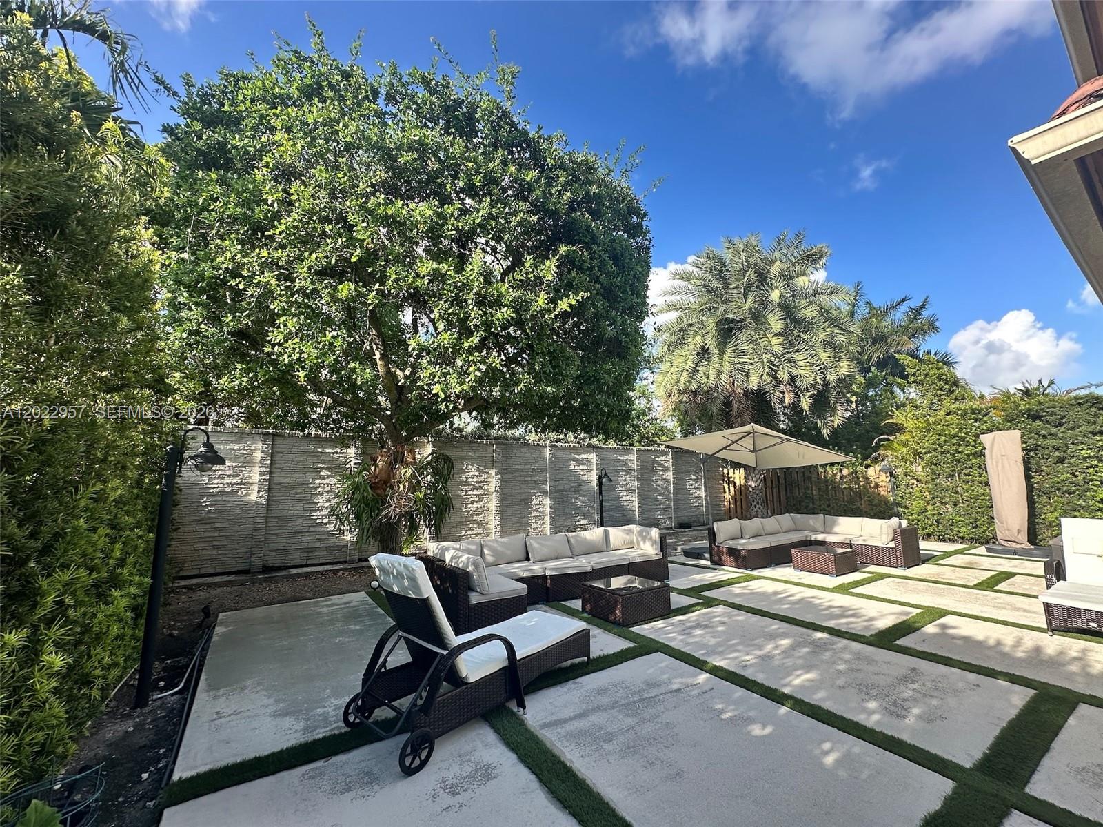 A backyard patio features concrete pavers, outdoor furniture, a large tree, and a privacy fence — 10919 NW 80th Ln, Doral FL 33178, DORAL, FL