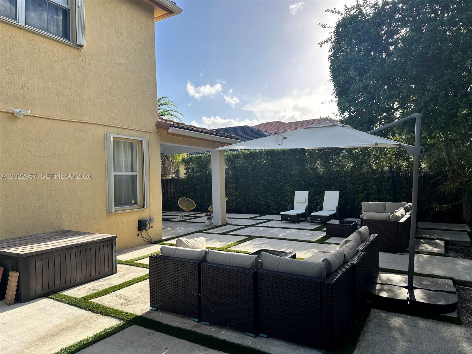 A backyard patio features a sectional sofa, lounge chairs, and a large umbrella on pavers — 10919 NW 80th Ln, Doral FL 33178, DORAL, FL