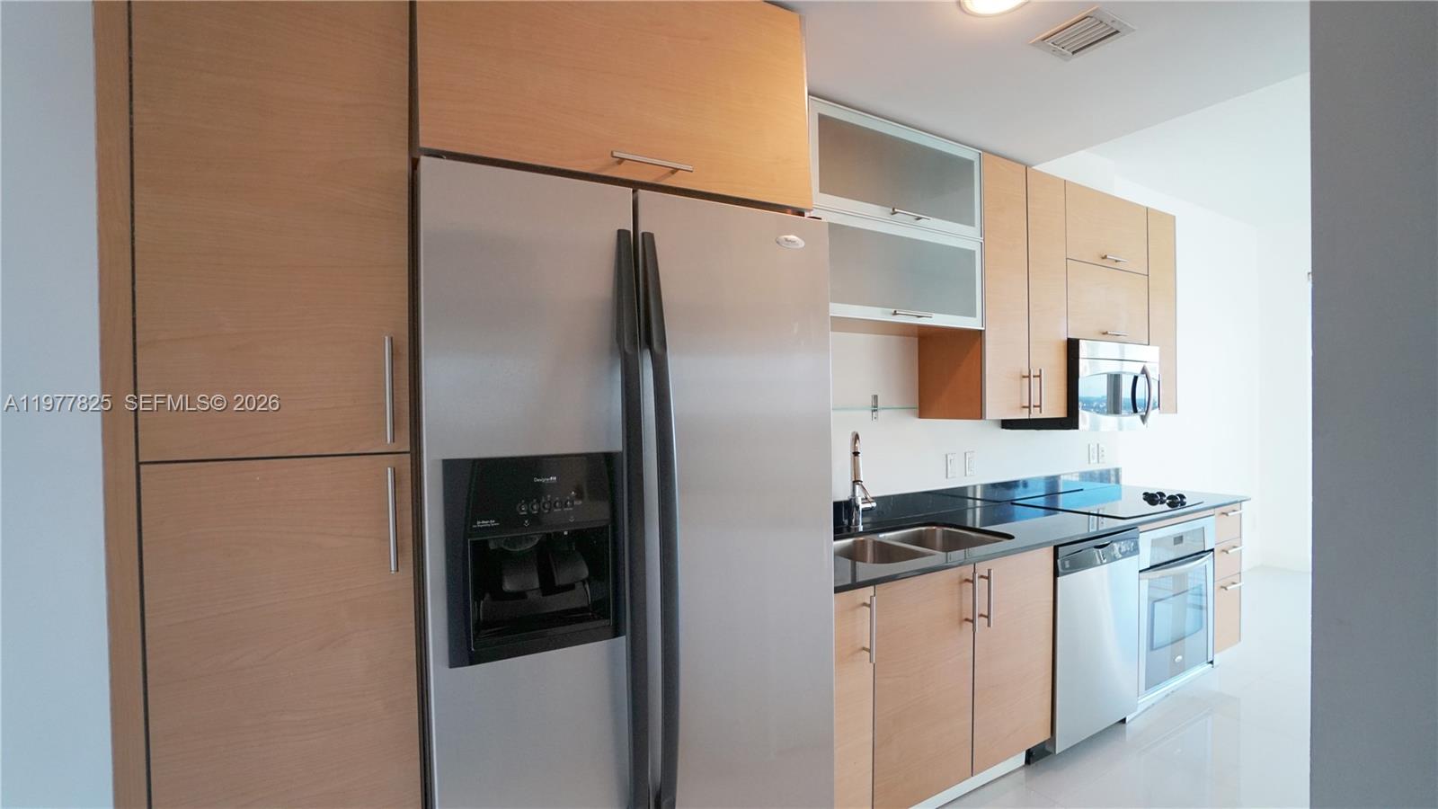 A modern kitchen features light wood cabinetry, stainless steel appliances, and black granite countertops — 60 SW 13th St # 2215, Miami FL 33130, MIAMI, FL