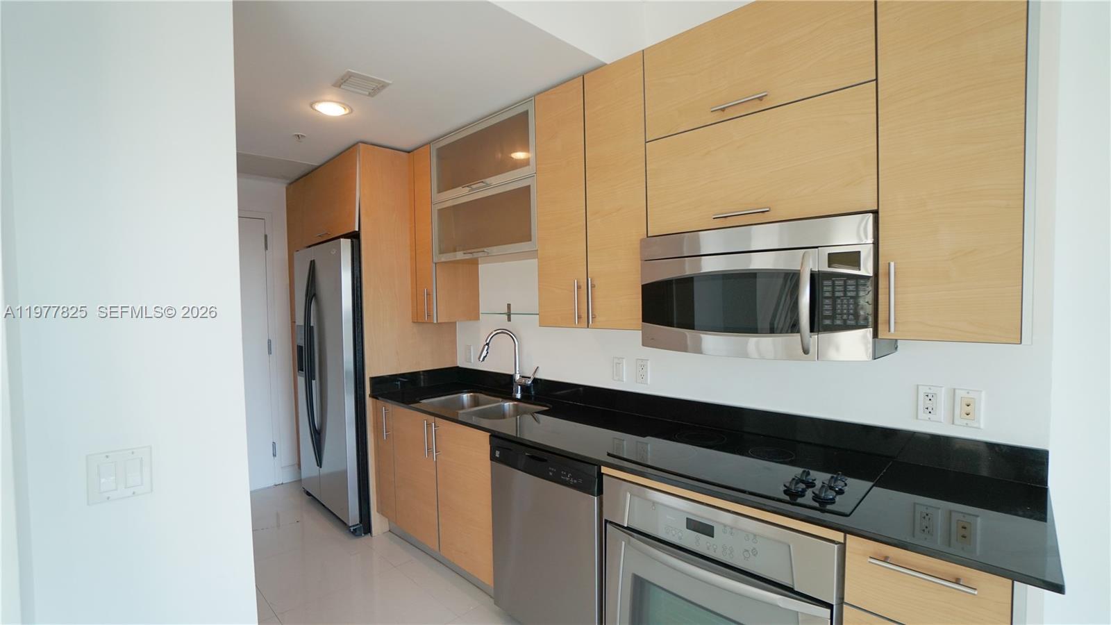 A kitchen features light wood cabinets, black countertops, and stainless steel appliances — 60 SW 13th St # 2215, Miami FL 33130, MIAMI, FL