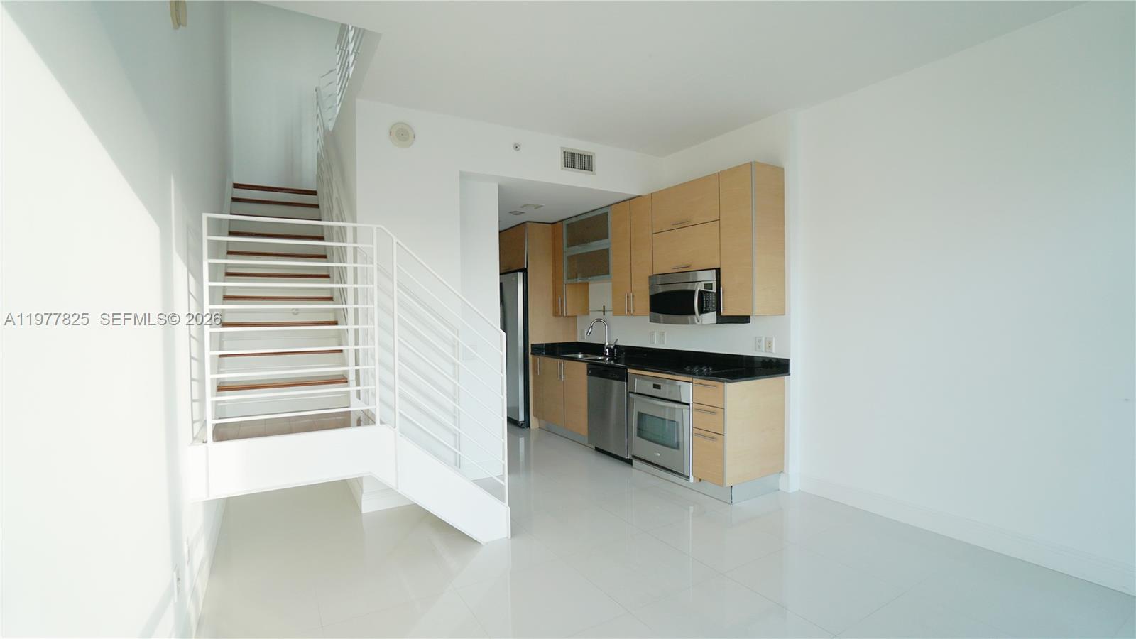 A modern kitchen with light wood cabinets and stainless steel appliances sits beside a staircase — 60 SW 13th St # 2215, Miami FL 33130, MIAMI, FL