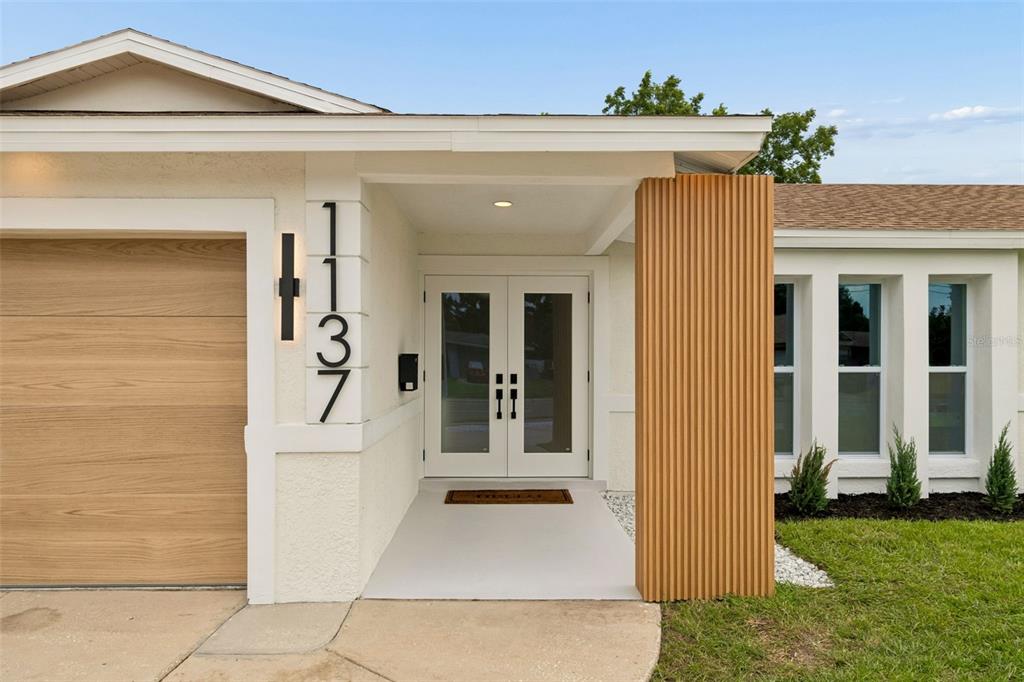 The exterior of a house features a white facade, a wood-slatted pillar, and double glass doors — 1137 54TH AVENUE S, ST PETERSBURG, FL