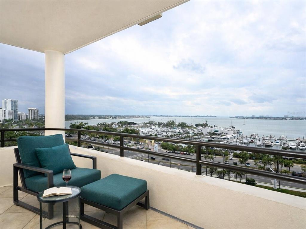 A balcony with a teal chair and ottoman overlooks a marina and city skyline — 1255 N GULFSTREAM AVENUE UNIT 1106, SARASOTA, FL