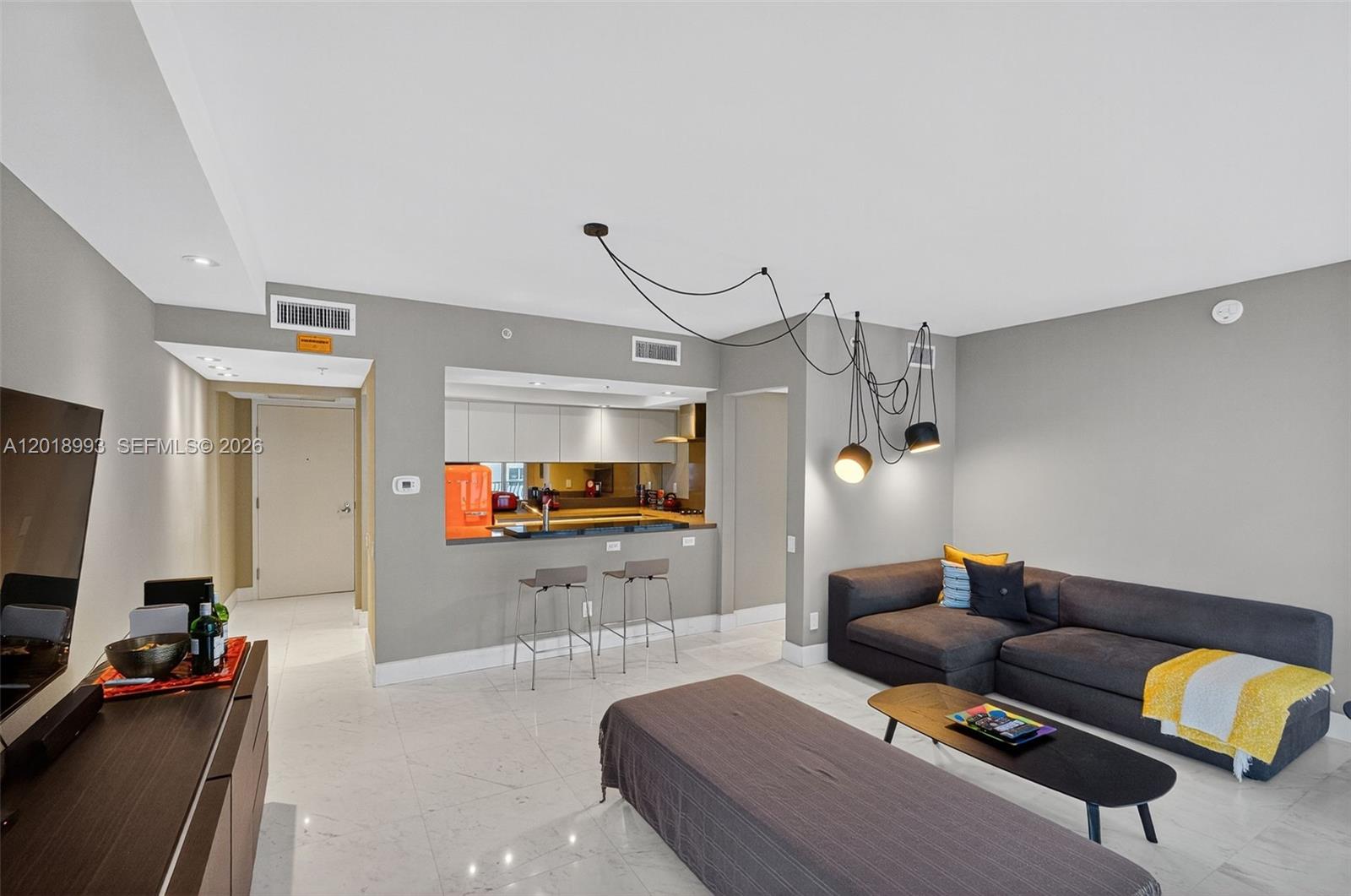 A modern living room features a grey sectional sofa, a kitchen pass-through, and pendant lighting — 1500 Ocean Dr # 507, Miami Beach FL 33139, MIAMI BEACH, FL