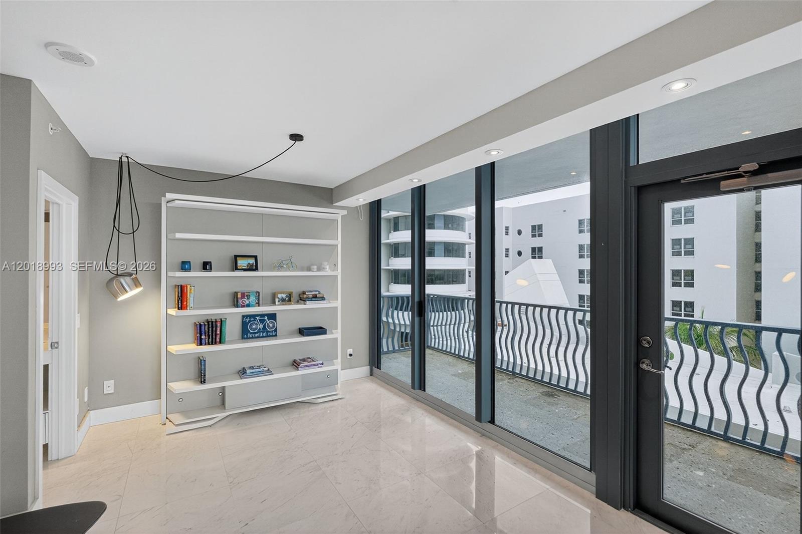 A room with light tile floors, a white bookshelf, and a balcony with metal railings — 1500 Ocean Dr # 507, Miami Beach FL 33139, MIAMI BEACH, FL