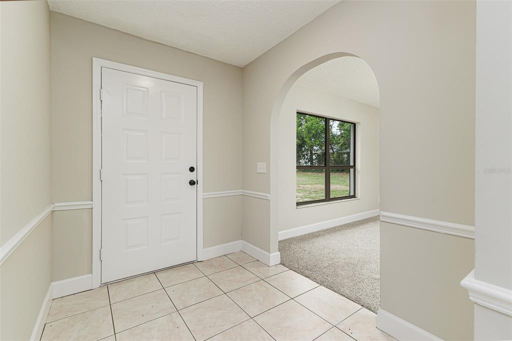 An entryway with tile flooring, a white door, and an arched opening to a carpeted room — 4052 LEHMAN COURT, LAKELAND, FL