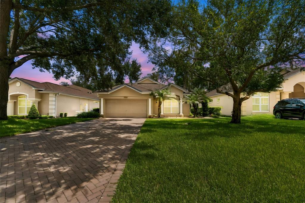 A single-story house with a paved driveway, a two-car garage, and mature trees in front — 12442 FOREST HIGHLANDS DRIVE, DADE CITY, FL