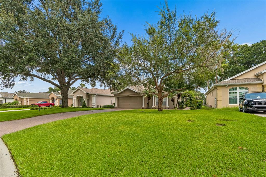 A suburban house with a paved driveway, green lawn, and large trees in the front yard — 12442 FOREST HIGHLANDS DRIVE, DADE CITY, FL