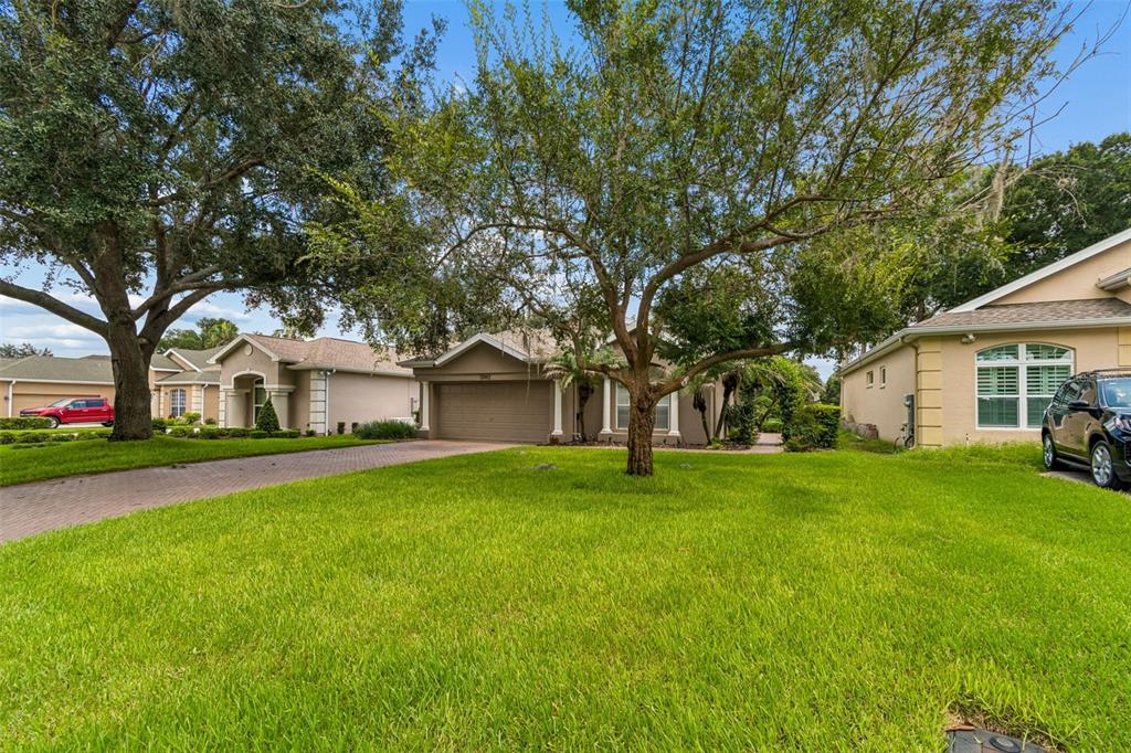 A suburban house with a brown garage, a large front lawn, and mature oak trees — 12442 FOREST HIGHLANDS DRIVE, DADE CITY, FL