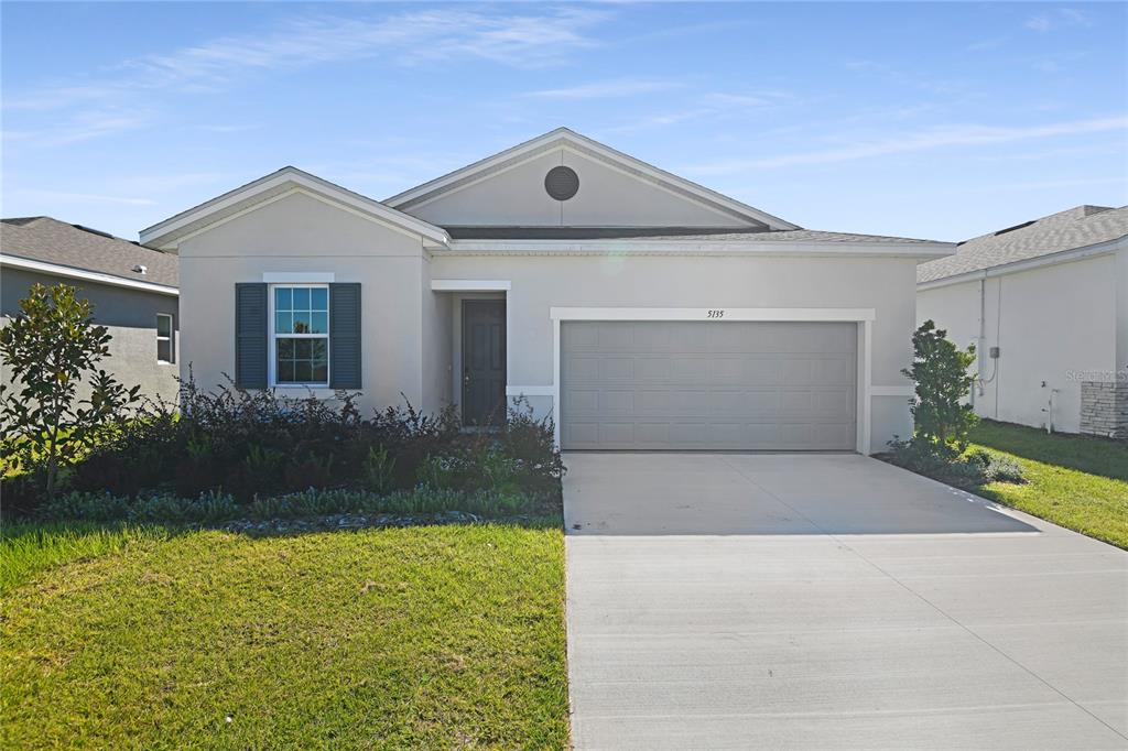 A single-story suburban house features a light-colored stucco exterior, a two-car garage, and landscaping — 5135 KINSLEY DRIVE, WINTER HAVEN, FL