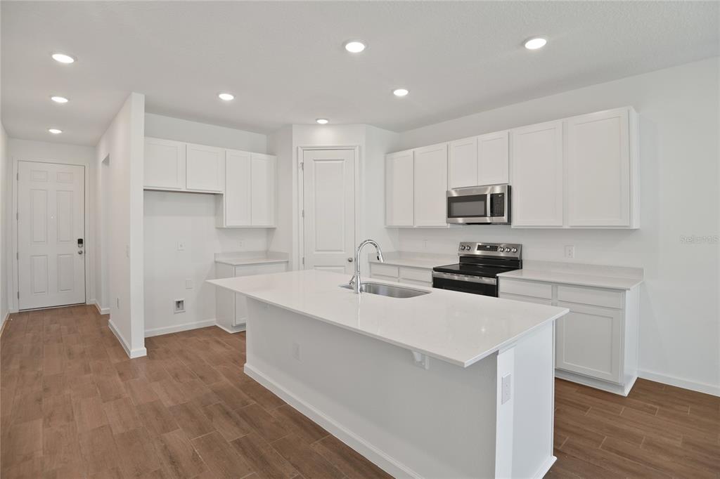 A modern kitchen features white cabinets, a central island with a sink, and wood-look flooring — 5135 KINSLEY DRIVE, WINTER HAVEN, FL