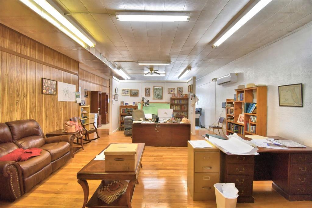 A spacious office room features wood-paneled walls, hardwood floors, multiple desks, and fluorescent lighting — 105 S SCENIC HIGHWAY, FROSTPROOF, FL