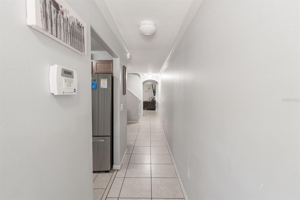 A hallway with light-colored tile flooring leads toward an arched doorway and a kitchen area — 10928 KEYS GATE DR, RIVERVIEW, FL