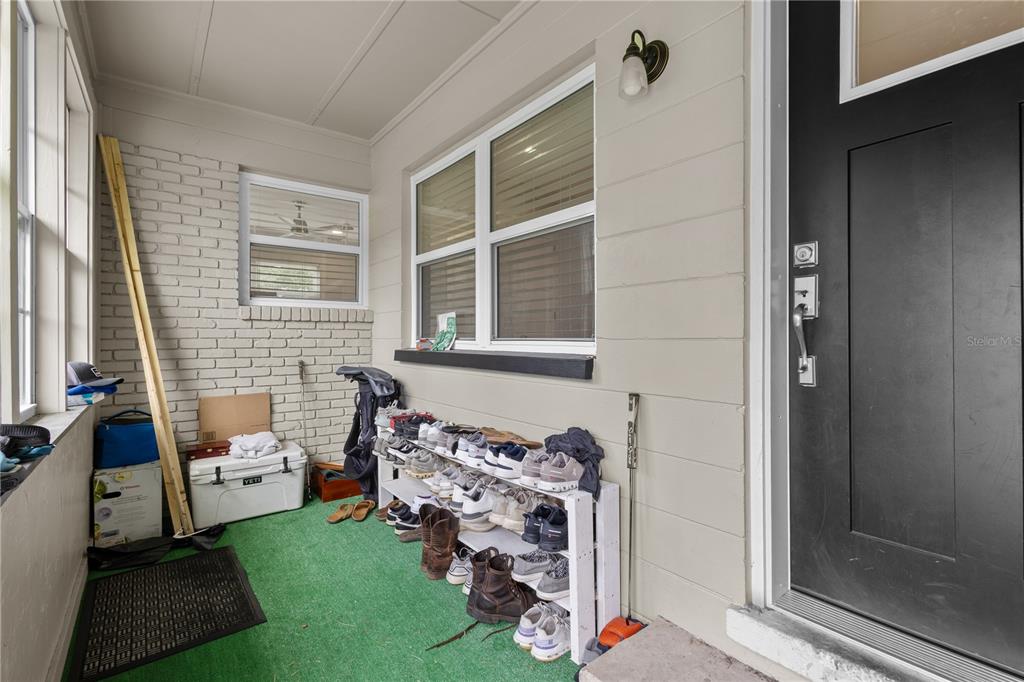 A covered porch features a white brick wall, a shoe rack, and a black front door — 805 NW 40TH TERRACE, GAINESVILLE, FL