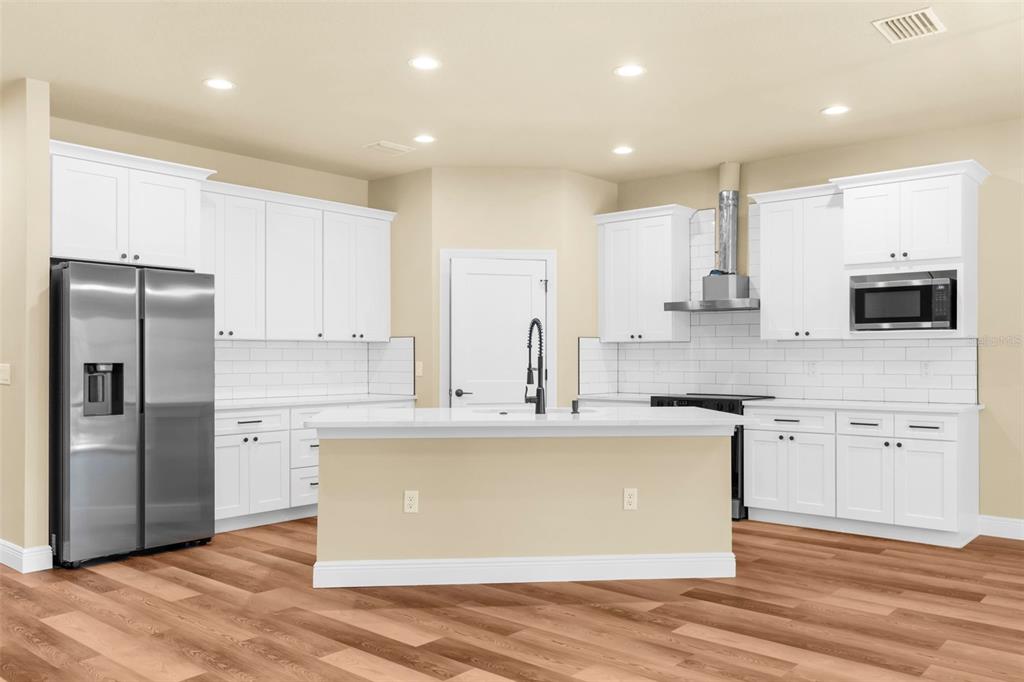 A modern kitchen features white cabinets, stainless steel appliances, a center island, and wood flooring — 16143 PENN STATE ROAD, WEEKI WACHEE, FL