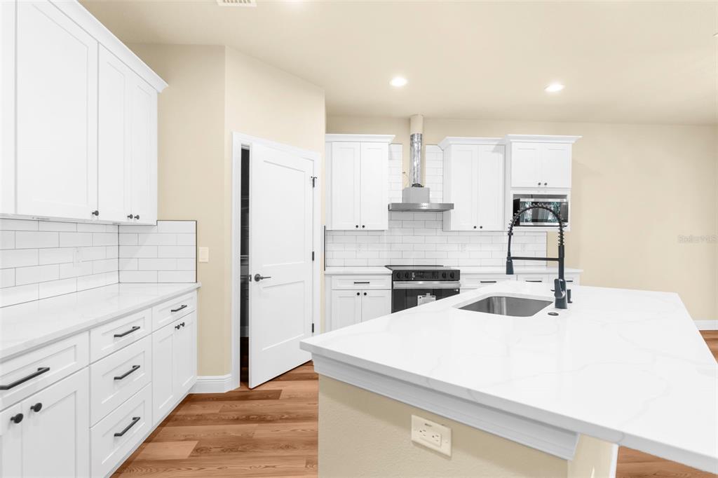 A modern kitchen features white cabinets, a quartz-topped island with a sink, and subway tile — 16143 PENN STATE ROAD, WEEKI WACHEE, FL