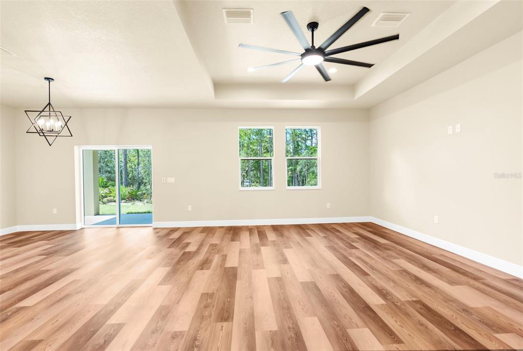 A spacious living area features light walls, wood-look flooring, a tray ceiling, and sliding glass doors — 16143 PENN STATE ROAD, WEEKI WACHEE, FL