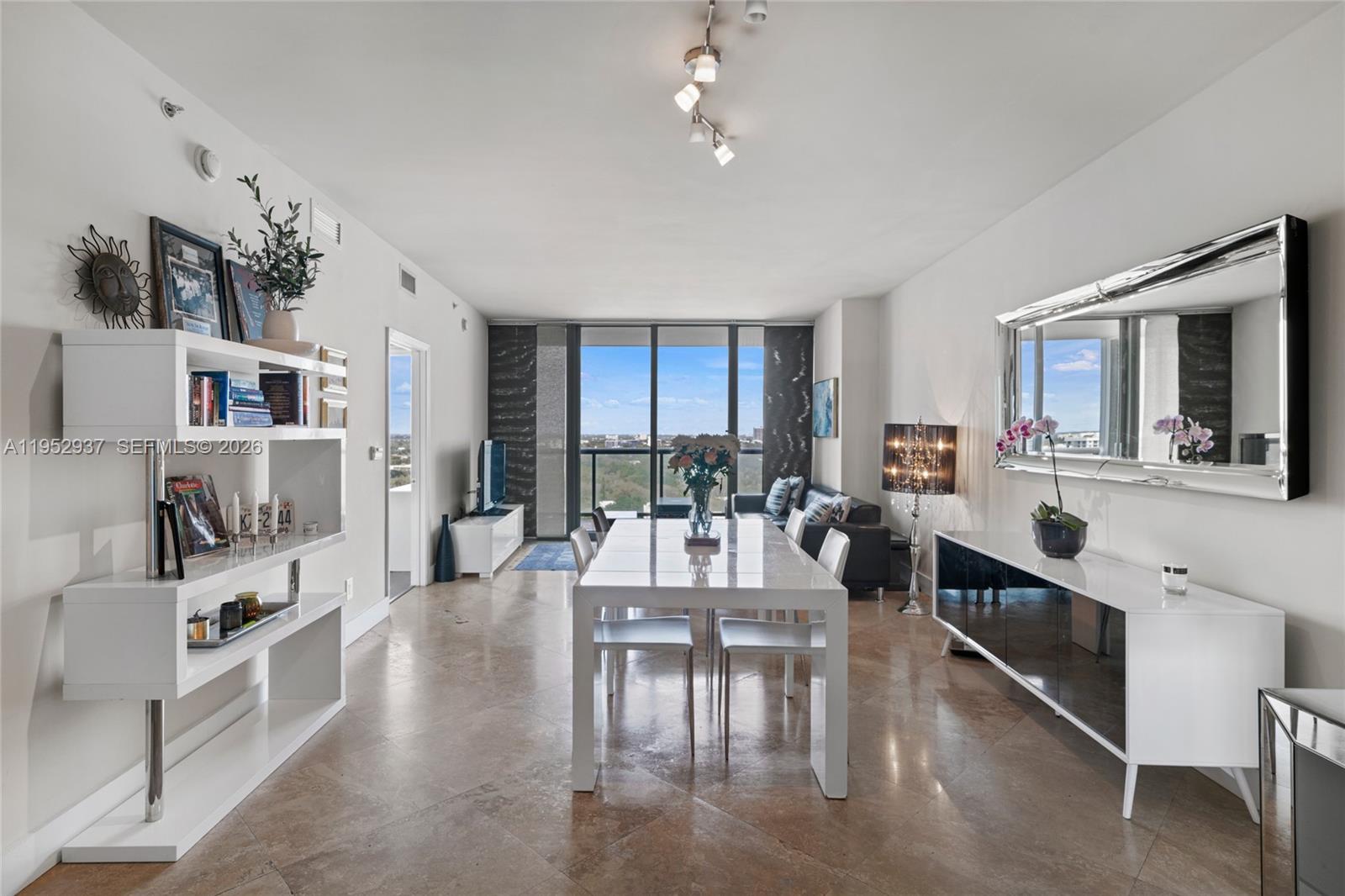 A modern dining and living area features white furniture, tile floors, and floor-to-ceiling windows — 601 NE 36th St # 1704, Miami FL 33137, MIAMI, FL