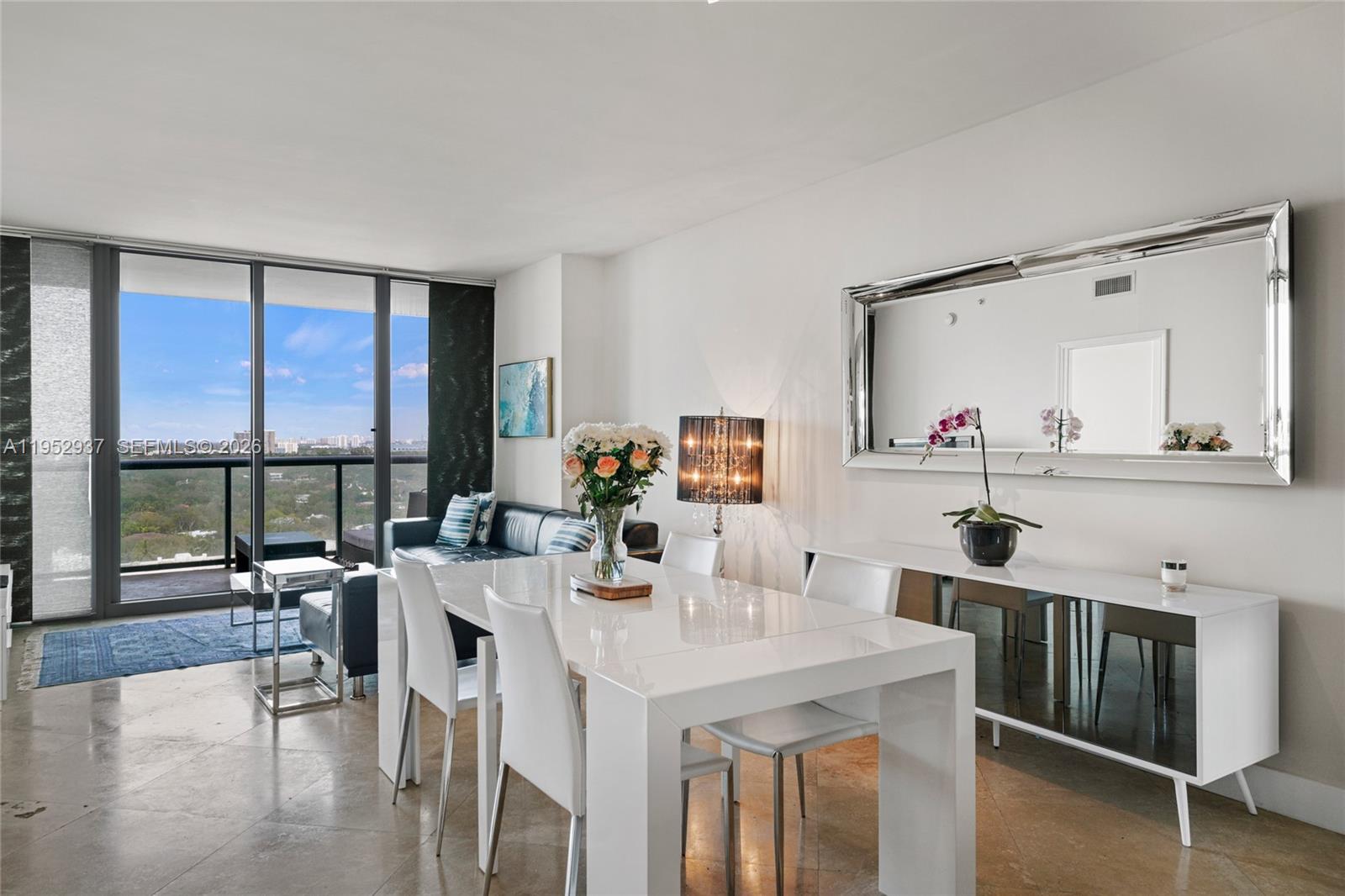 A modern dining area with a white table and chairs sits before a balcony view — 601 NE 36th St # 1704, Miami FL 33137, MIAMI, FL