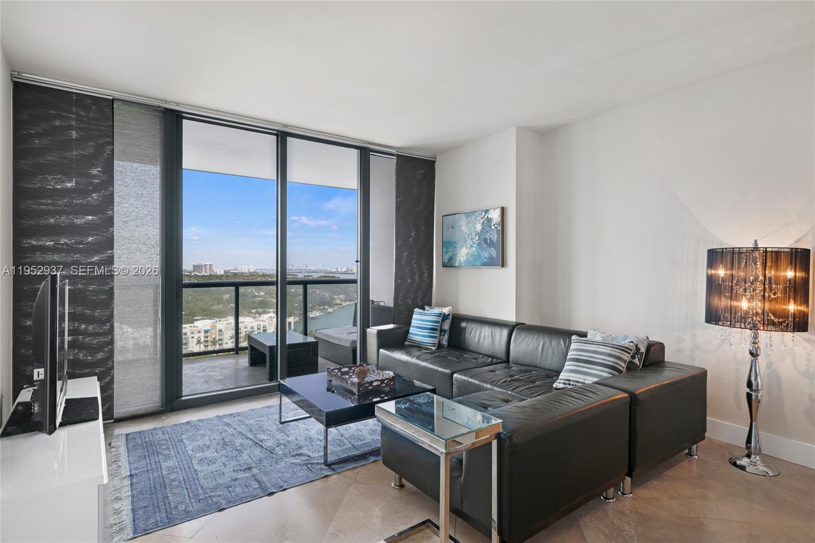 A living room features a black leather sectional, a glass coffee table, and floor-to-ceiling windows — 601 NE 36th St # 1704, Miami FL 33137, MIAMI, FL