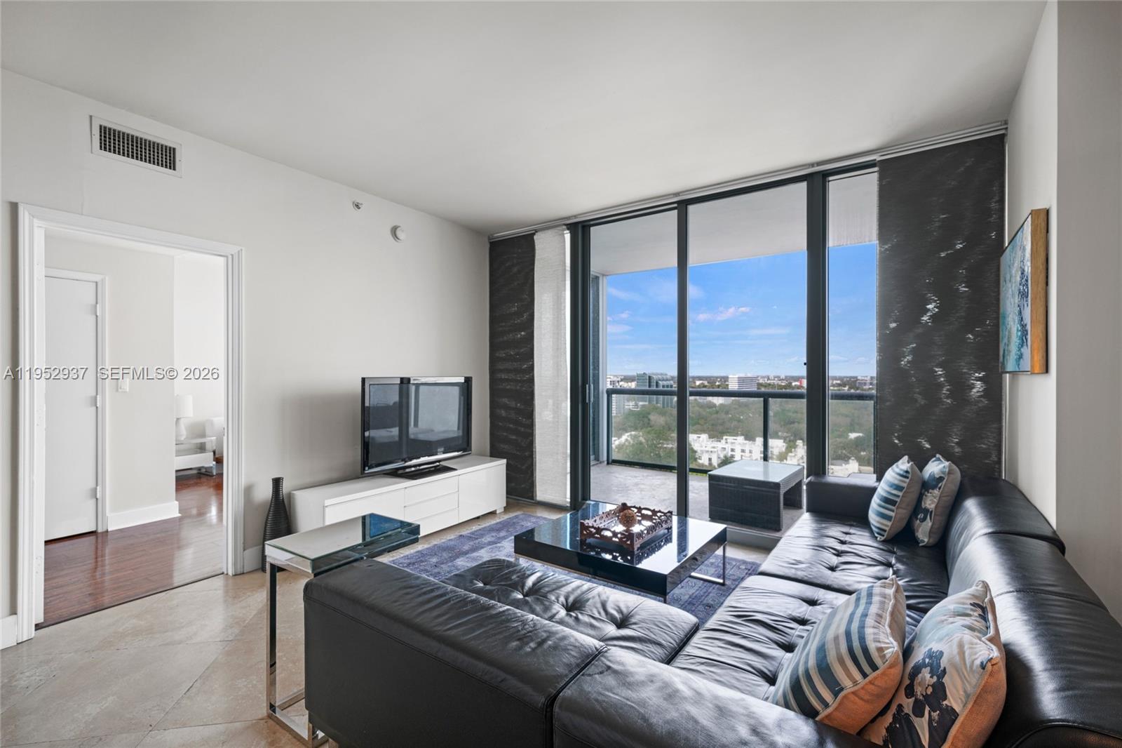 A living room features a black leather sectional, a glass coffee table, and a balcony view — 601 NE 36th St # 1704, Miami FL 33137, MIAMI, FL