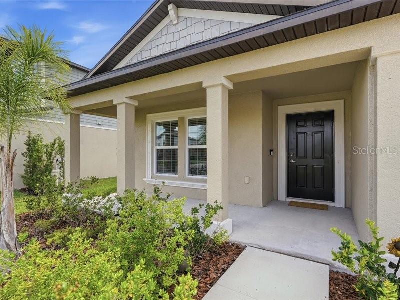 The exterior of a house features a covered porch, a black front door, and landscaping — 12032 BLUE DIAMOND TRAIL, PARRISH, FL