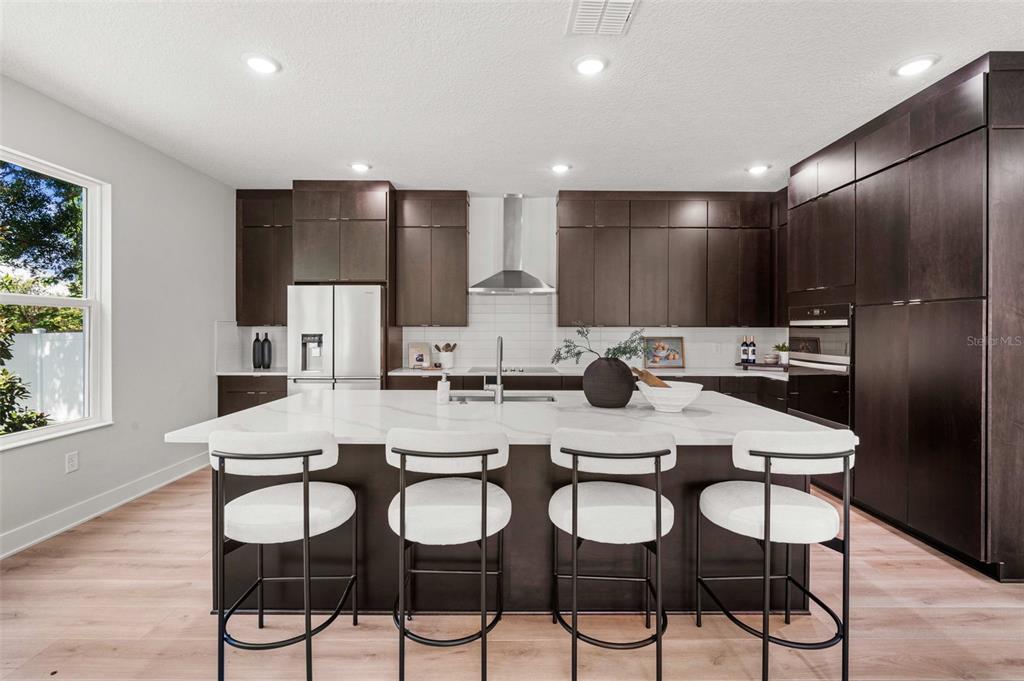 A modern kitchen features dark cabinetry, a large white island, and four bar stools — 3310 W ROGERS AVENUE, TAMPA, FL