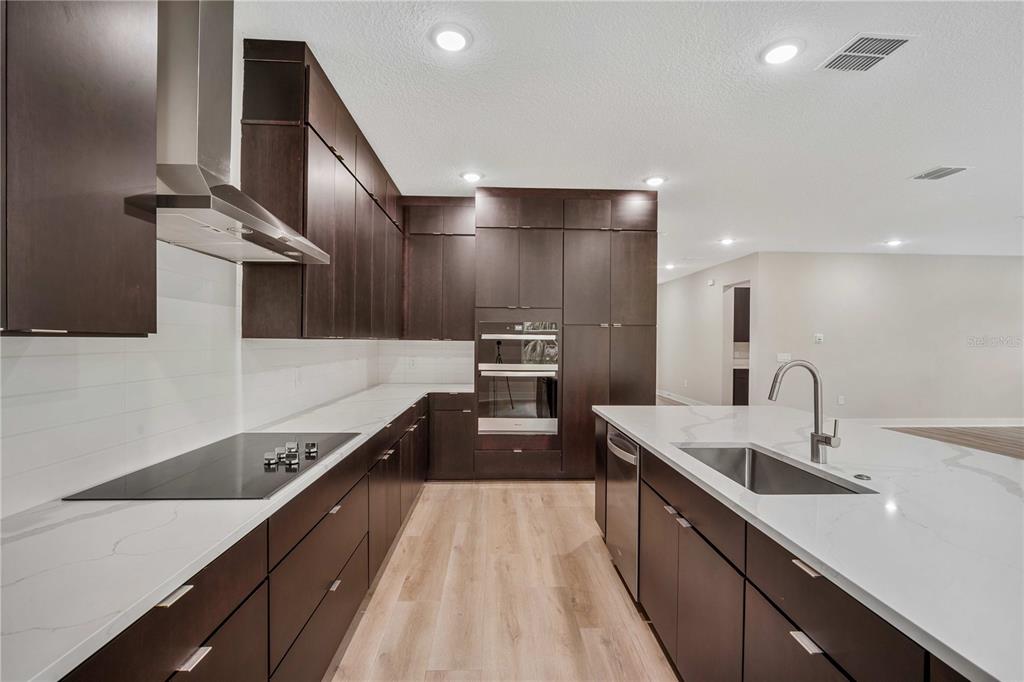 A modern kitchen features dark wood cabinetry, white countertops, stainless steel appliances, and wood flooring — 3310 W ROGERS AVENUE, TAMPA, FL