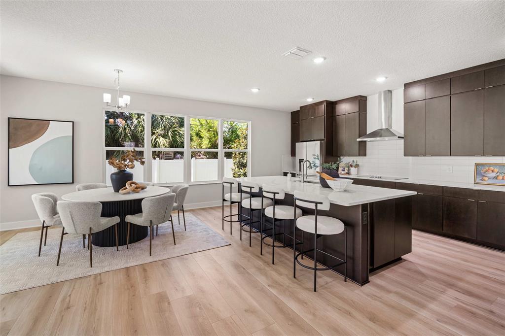 A modern kitchen and dining area feature dark cabinetry, a large island, and light flooring — 3310 W ROGERS AVENUE, TAMPA, FL