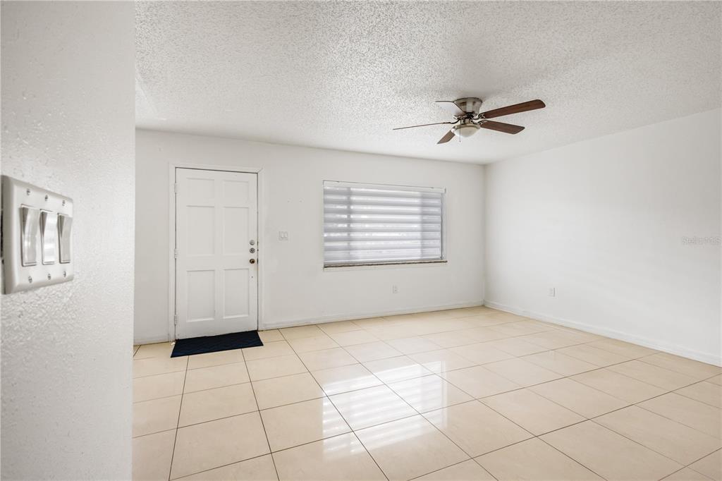 A bright, empty living room features white walls, light-colored tile flooring, and a ceiling fan — 1831 BOUGH AVENUE UNIT 1, CLEARWATER, FL