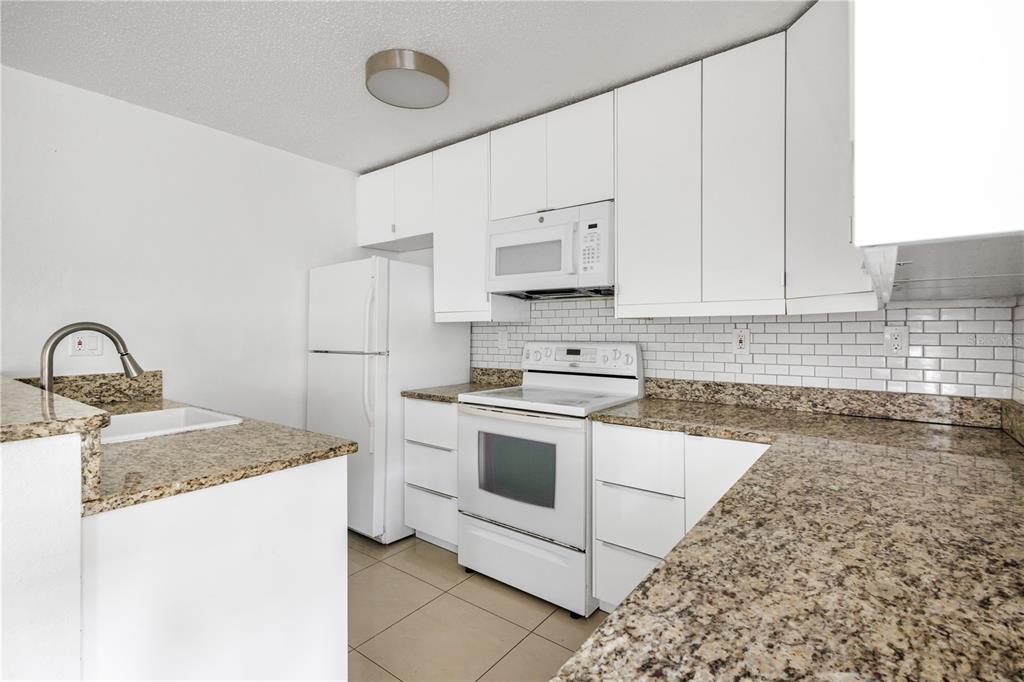 A kitchen features white cabinets, granite countertops, a white appliance suite, and a subway tile backsplash — 1831 BOUGH AVENUE UNIT 1, CLEARWATER, FL