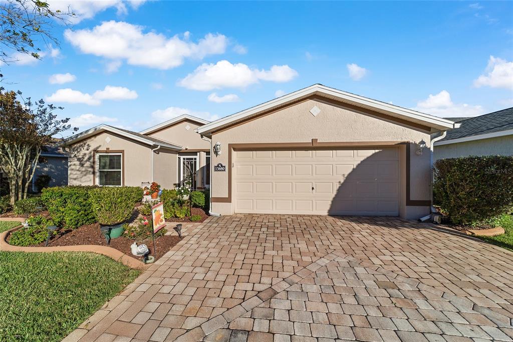 A single-story house with a beige stucco exterior, a two-car garage, and a paver driveway — 15680 SW 13TH CIRCLE, OCALA, FL