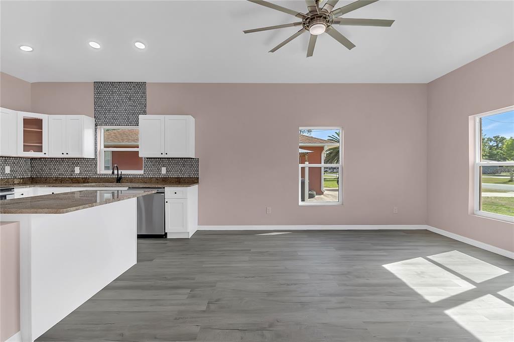 A kitchen with white cabinets, granite countertops, and gray flooring opens to a dining area — 707 HAMILTON STREET, NEW SMYRNA BEACH, FL