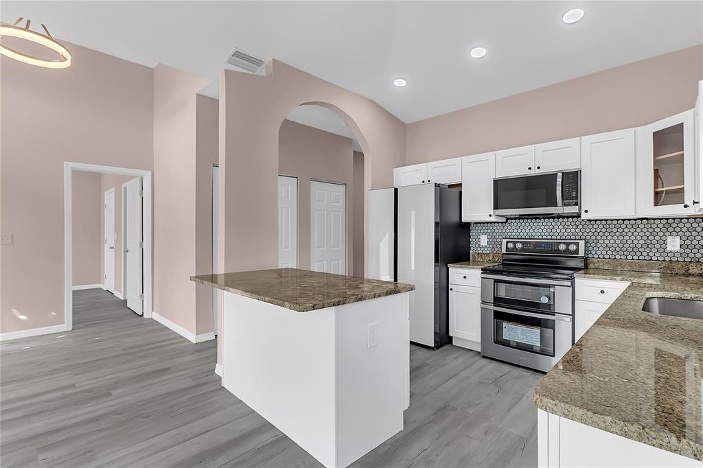 A kitchen features white cabinets, granite countertops, stainless steel appliances, and gray wood-look flooring — 707 HAMILTON STREET, NEW SMYRNA BEACH, FL