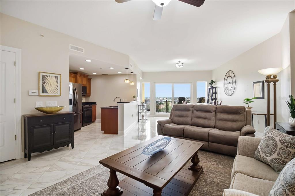 An open-concept living room and kitchen with tile floors, a brown sofa, and balcony views — 501 HABEN BOULEVARD UNIT 605, PALMETTO, FL