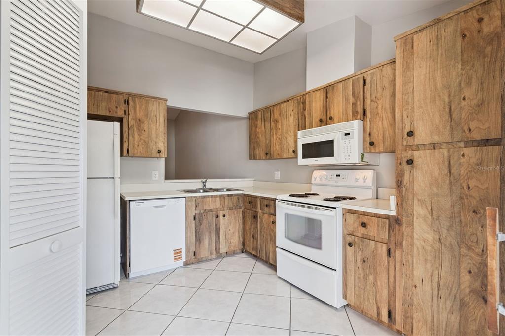 A kitchen with rustic wood cabinets, white appliances, and light-colored tile flooring — 419 WARRENTON ROAD UNIT 419, WINTER PARK, FL