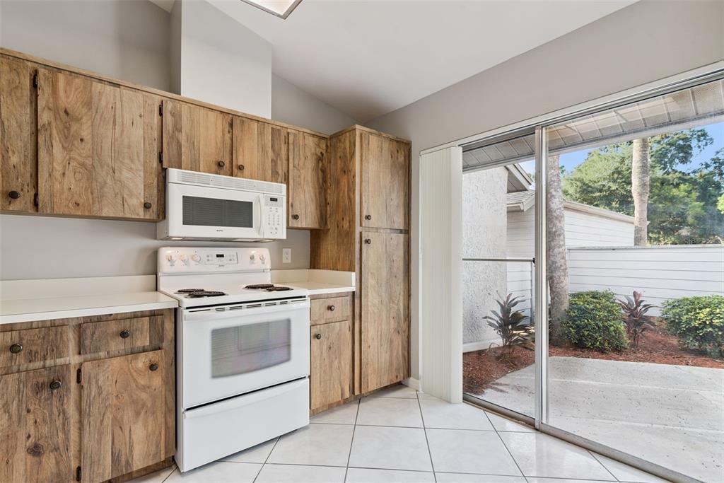 A kitchen features wood-grain cabinets, white appliances, tile flooring, and a sliding glass door — 419 WARRENTON ROAD UNIT 419, WINTER PARK, FL